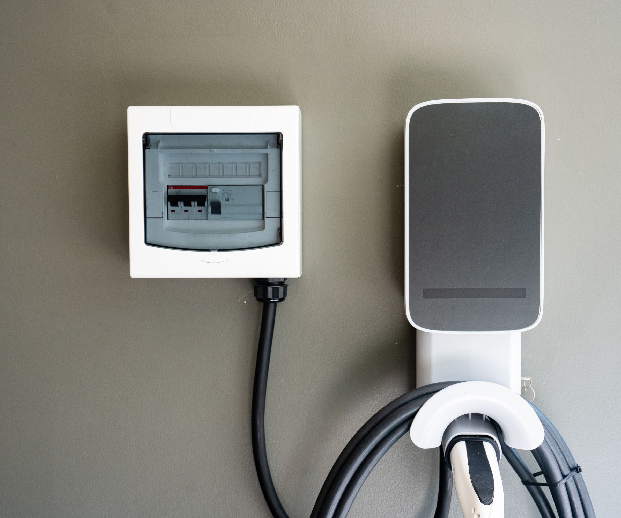 Une borne de recharge pour véhicule électrique soigneusement organisée et montée sur un mur, dotée d'une unité de commande et d'un câble spiralé, idéale pour la recharge de véhicules électriques à domicile.