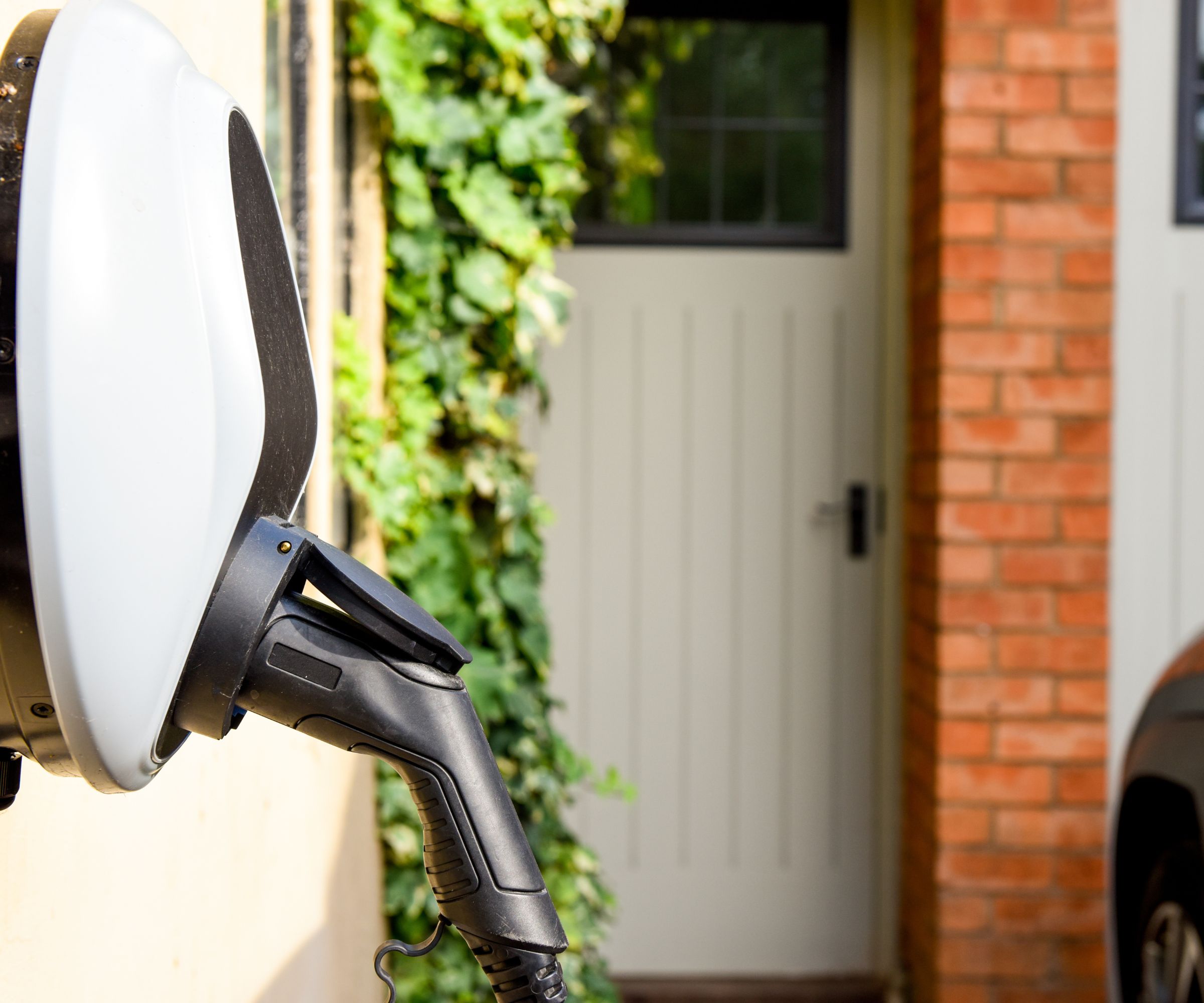 Un point de recharge pour voiture électrique fixé au mur d'une maison avec une prise noire. Une porte d'entrée floue en arrière-plan